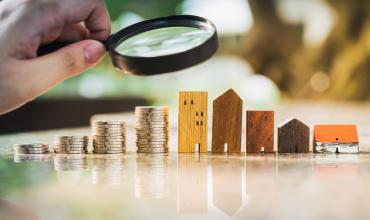 a hand holding a magnifying glass over Wooden toy houses 