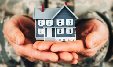 Person in a military uniform holding a little blue house