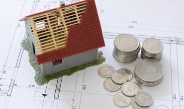 A miniature house with a roof being built next to some change on top of home plans