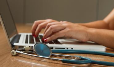 A stethoscope laying next to a person typing on a computer