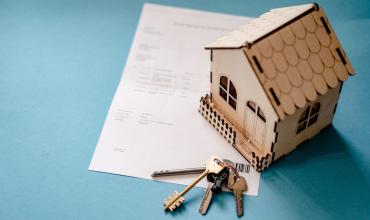 A small wooden house on top of a piece of paper with house keys next to it