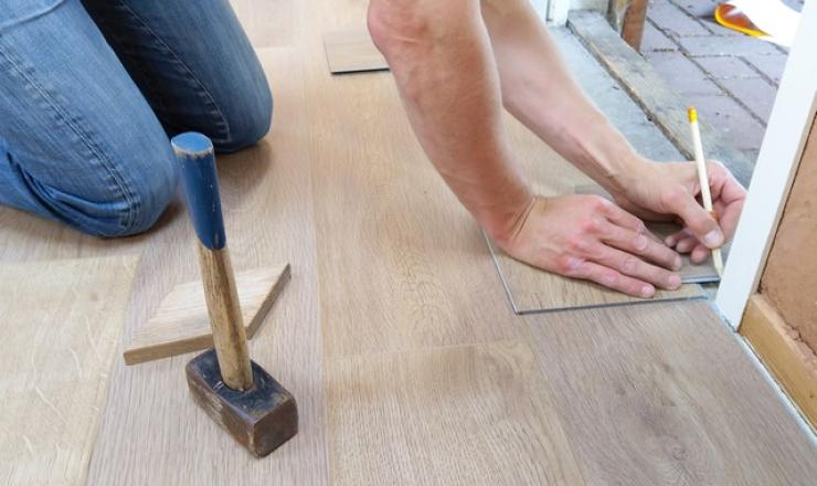 A person fixing a door on their hands and knees with a hammer next to them