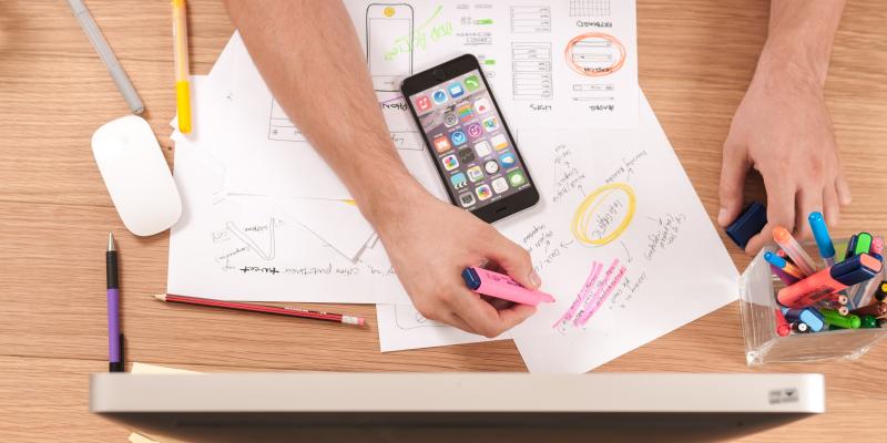 A hand writing on paper on a desk with a phone next to it