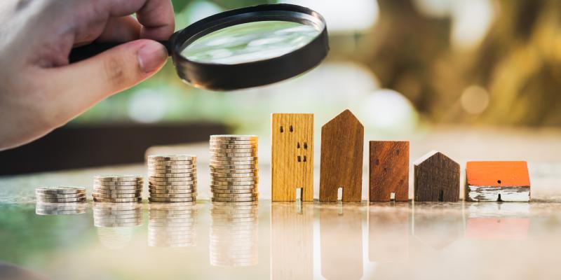 a hand holding a magnifying glass over Wooden toy houses 