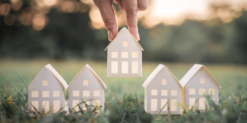 Paper houses being placed on the grass by a hand above