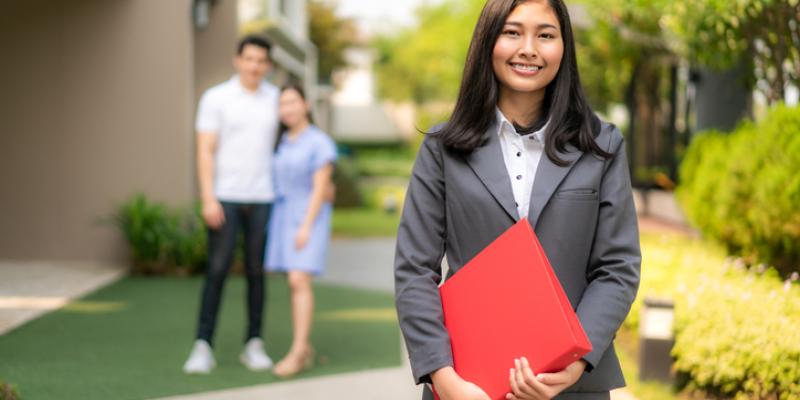 A woman holding a red folder standing in front of a couple that just bought a home