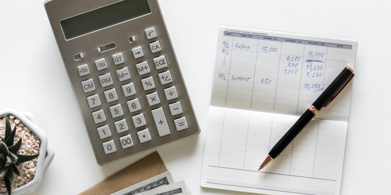 a table with a calculator, checkbook and pen