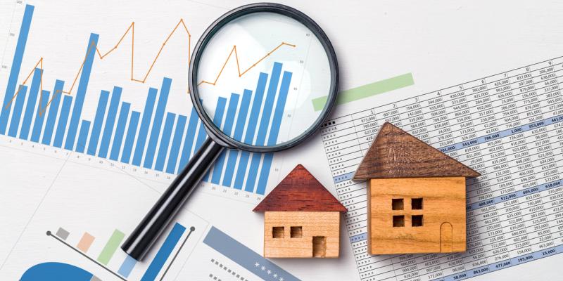 Two little wooden houses and a magnifying glass over papers with graphs and charts on them