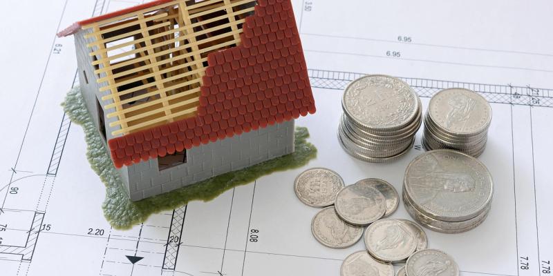 A miniature house with a roof being built next to some change on top of home plans