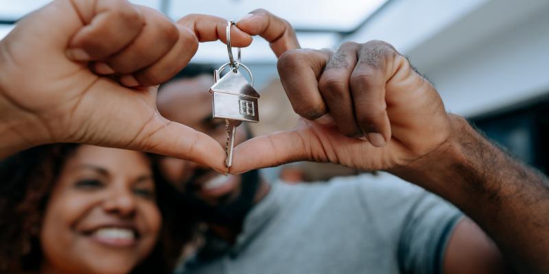 Couple holding up their house keys making a heart shape with their fingers